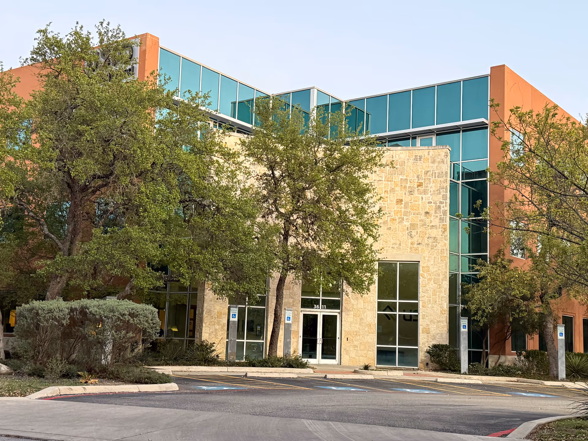 Exterior view of a modern building with glass walls, stone facade, and trees.