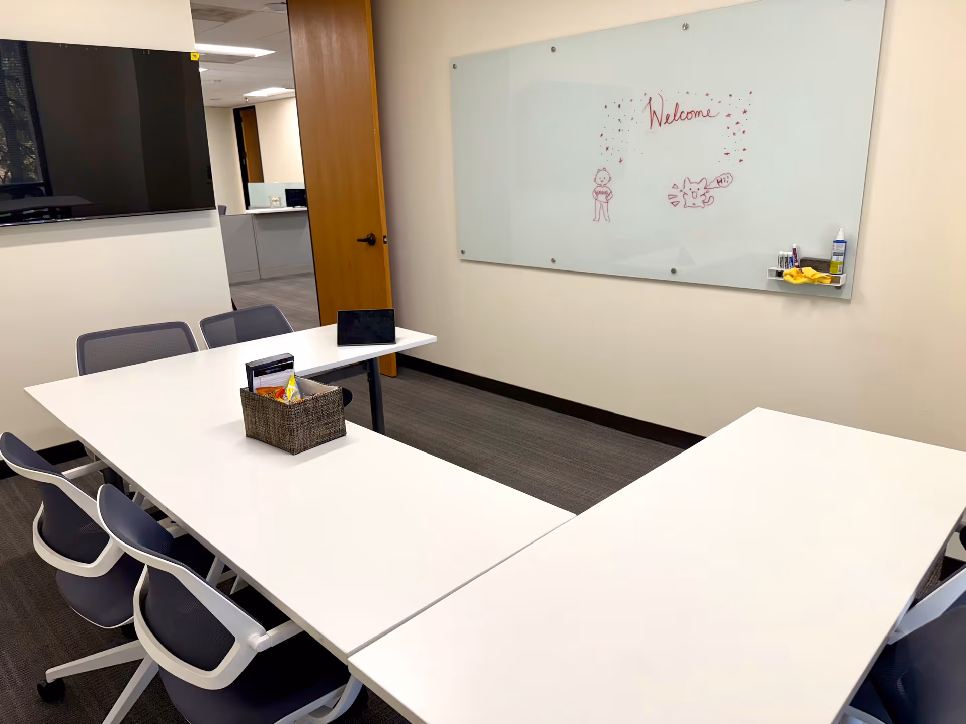 Bright conference room with white tables arranged in a U, a whiteboard, and chairs.