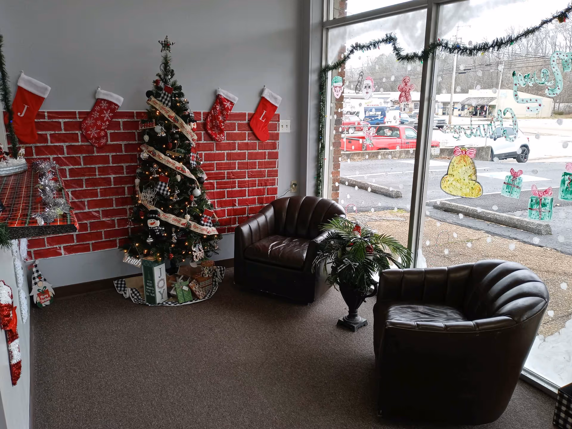 Cozy waiting area with Christmas tree, stockings, brick-pattern wall, and two leather chairs.