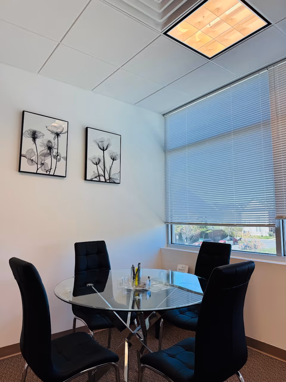 A glass round table with four black cushioned chairs in an office-like conference room.
