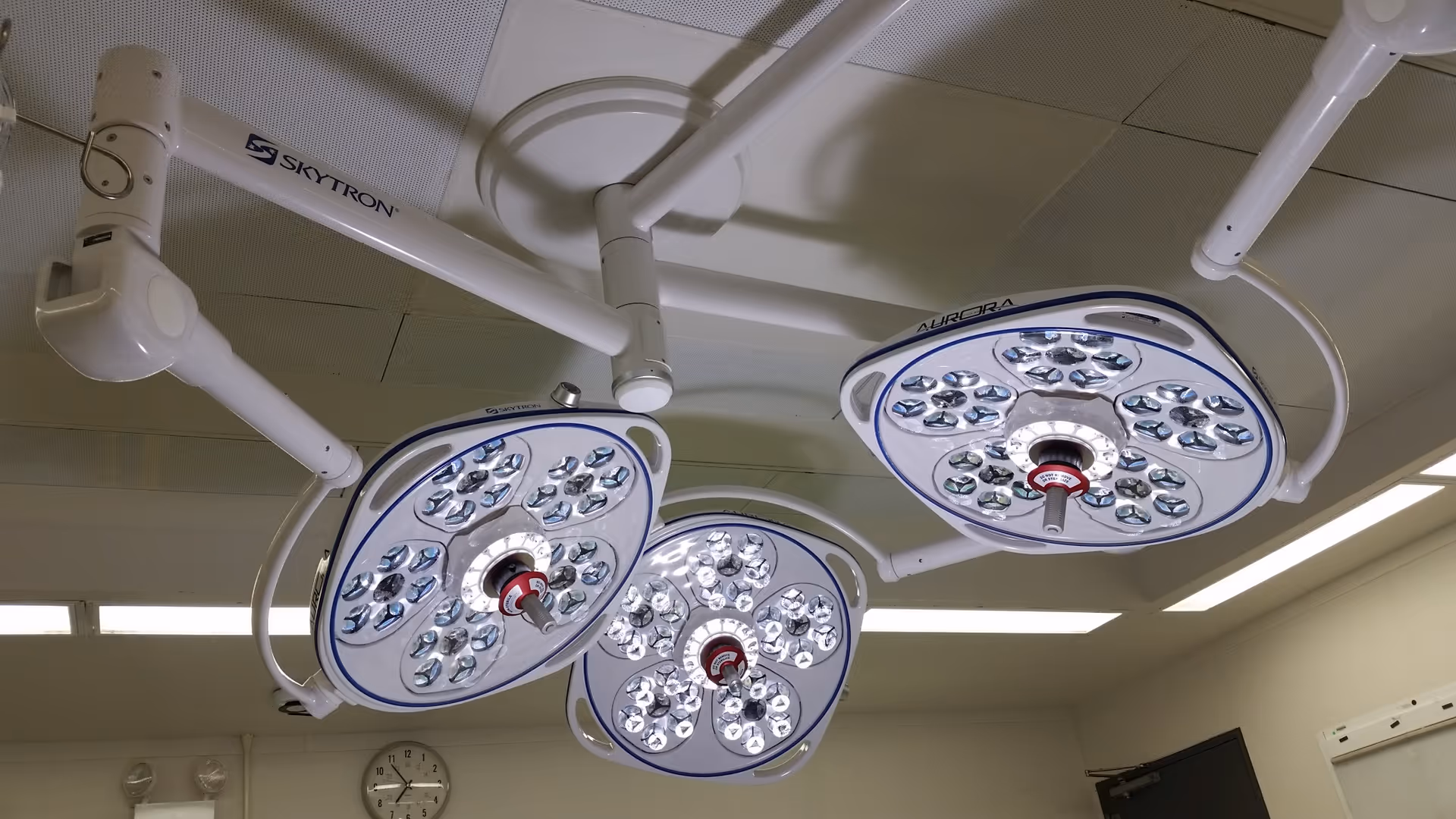Three overhead surgical lights hang from the ceiling in a sterile operating room.