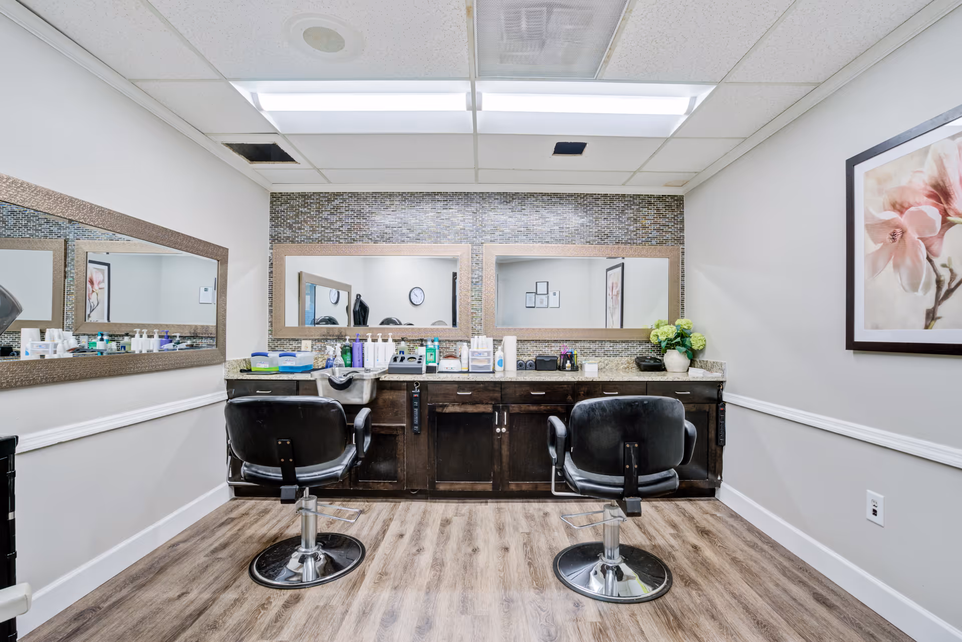 A senior living facility hair salon with two chairs, mirrors, and a tiled backsplash.