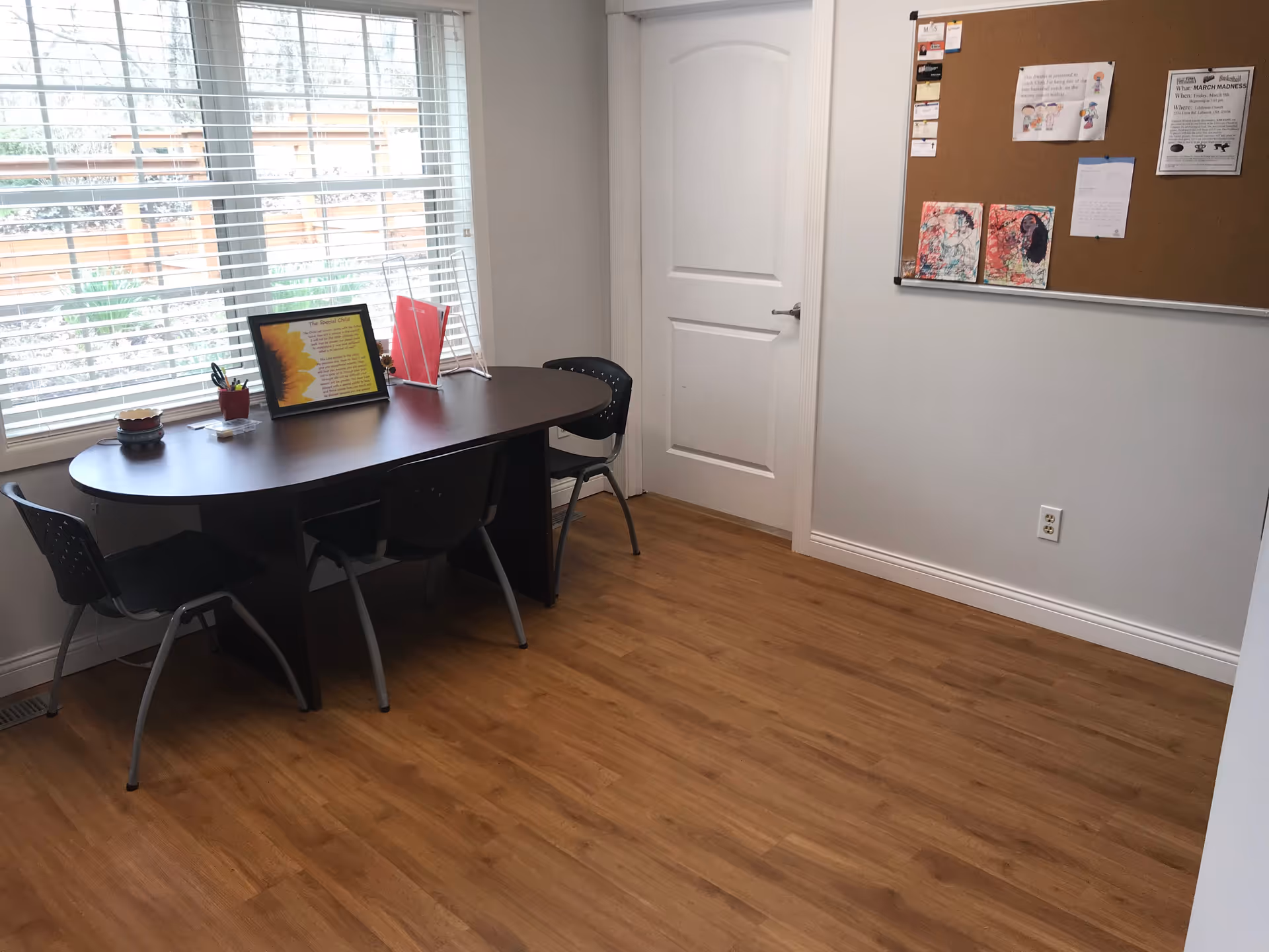 Curved desk with chairs, bulletin board, and a large window in a small interior room.