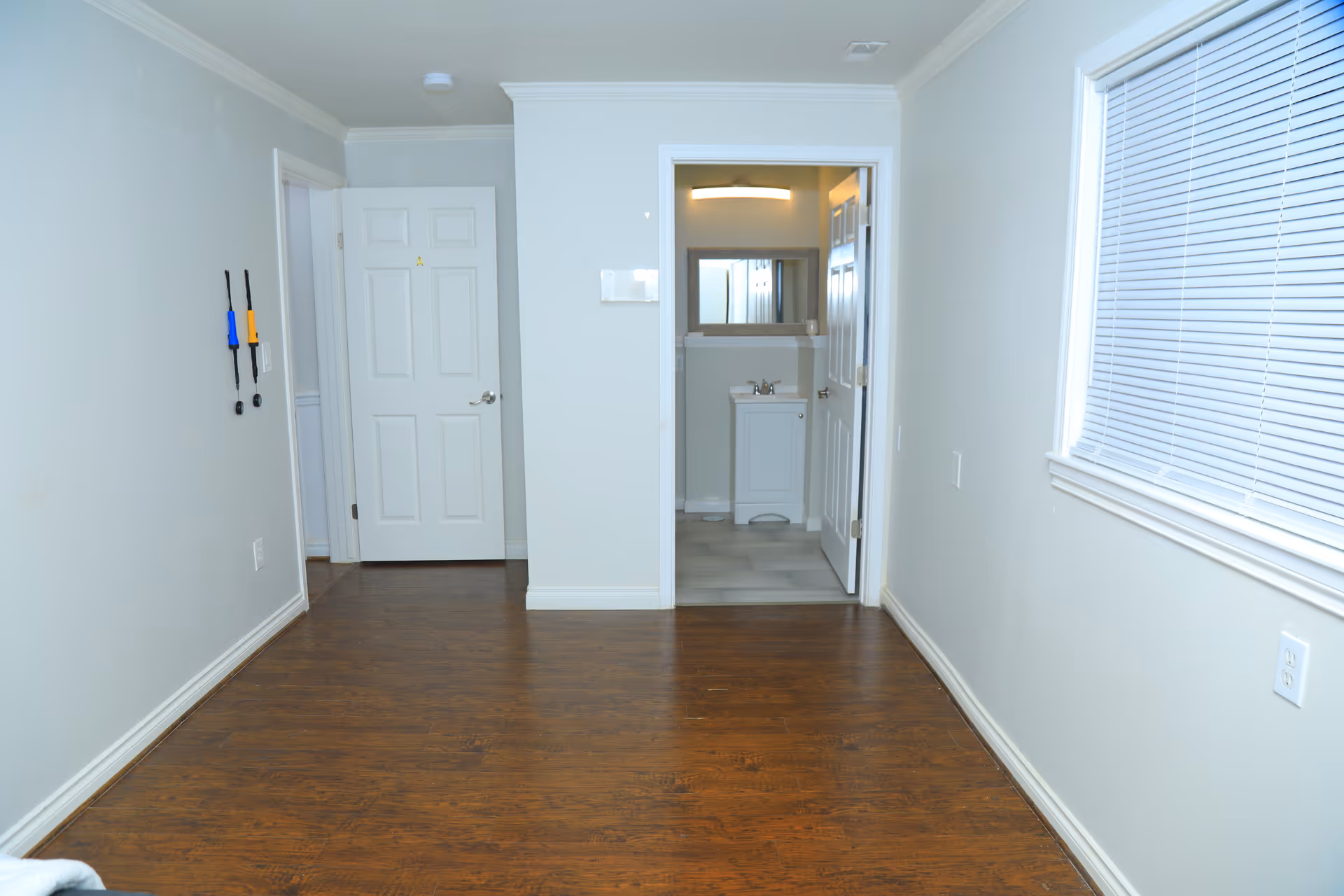 Bright hallway in a senior living facility with a bathroom doorway and window blinds.