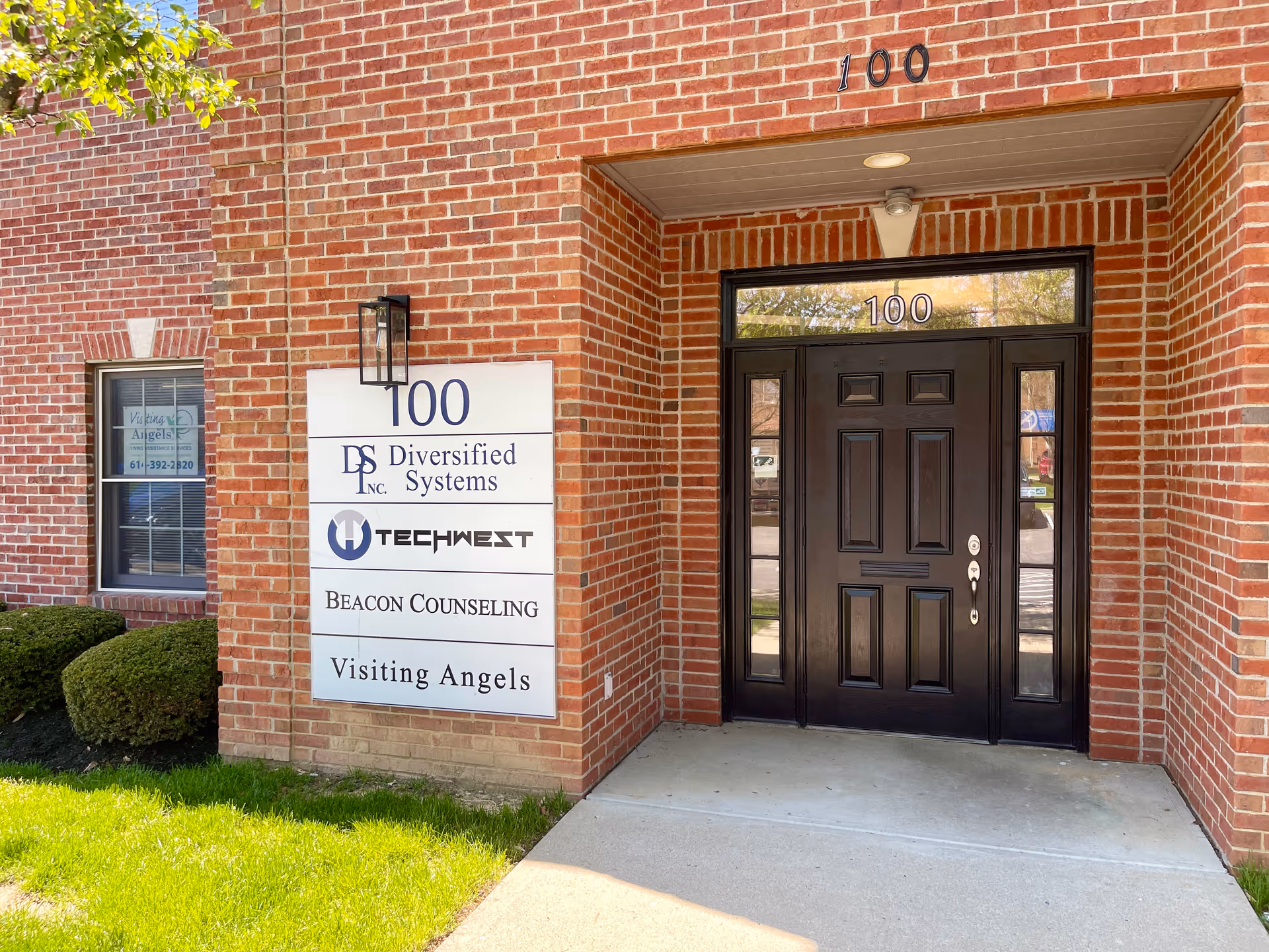 Brick building entrance with a dark door and a multi-brand sign beside it.