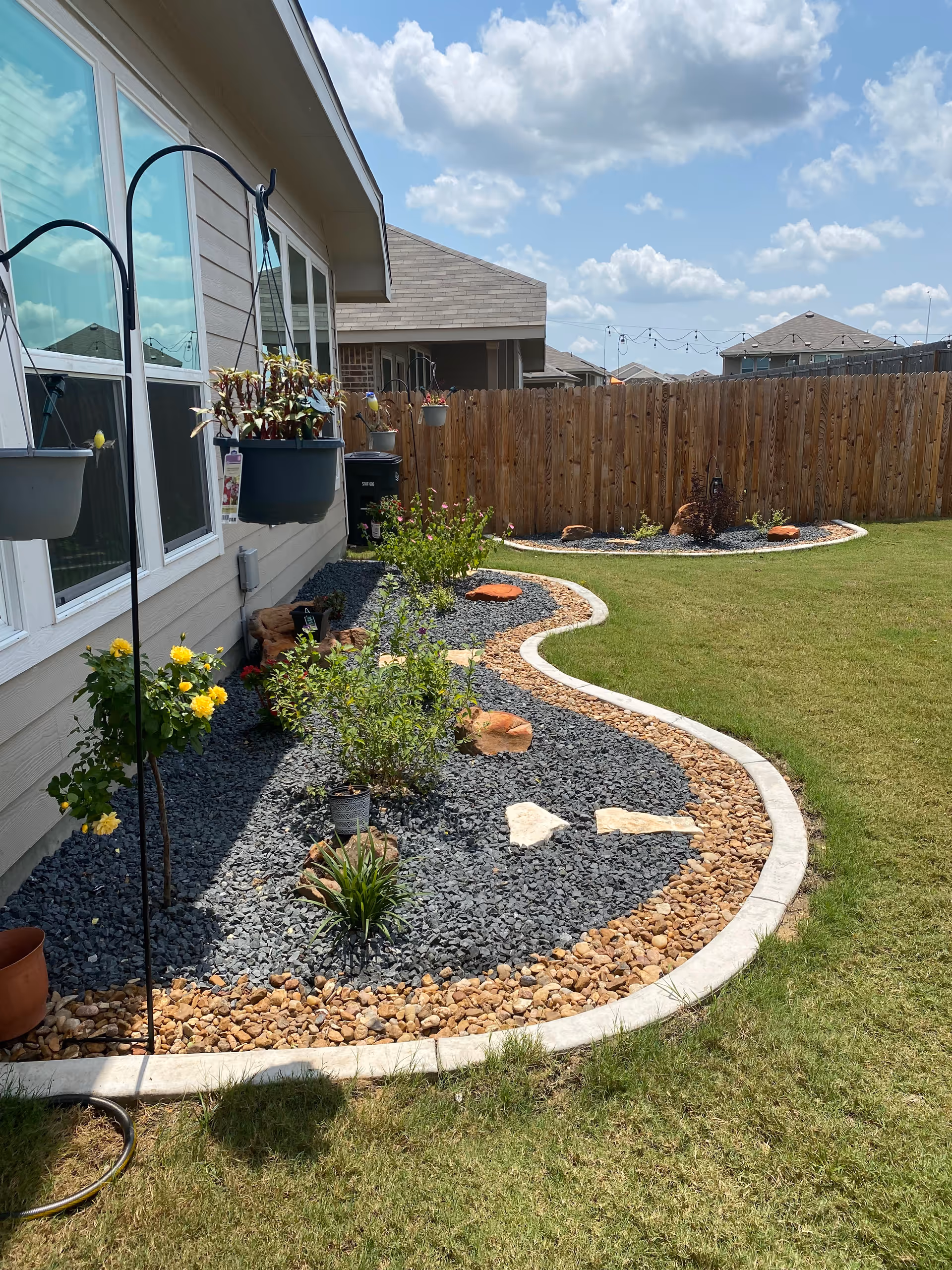 Backyard garden along the house with rock mulch, plants, and hanging planters.