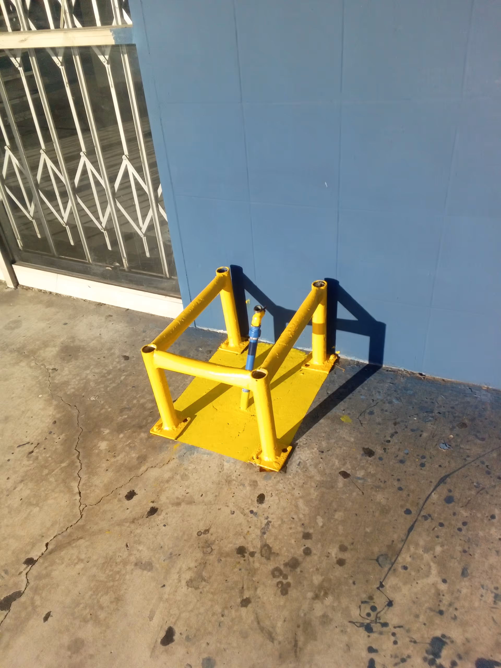 Yellow metal railing anchored to a square base sits on cracked concrete beside a blue wall