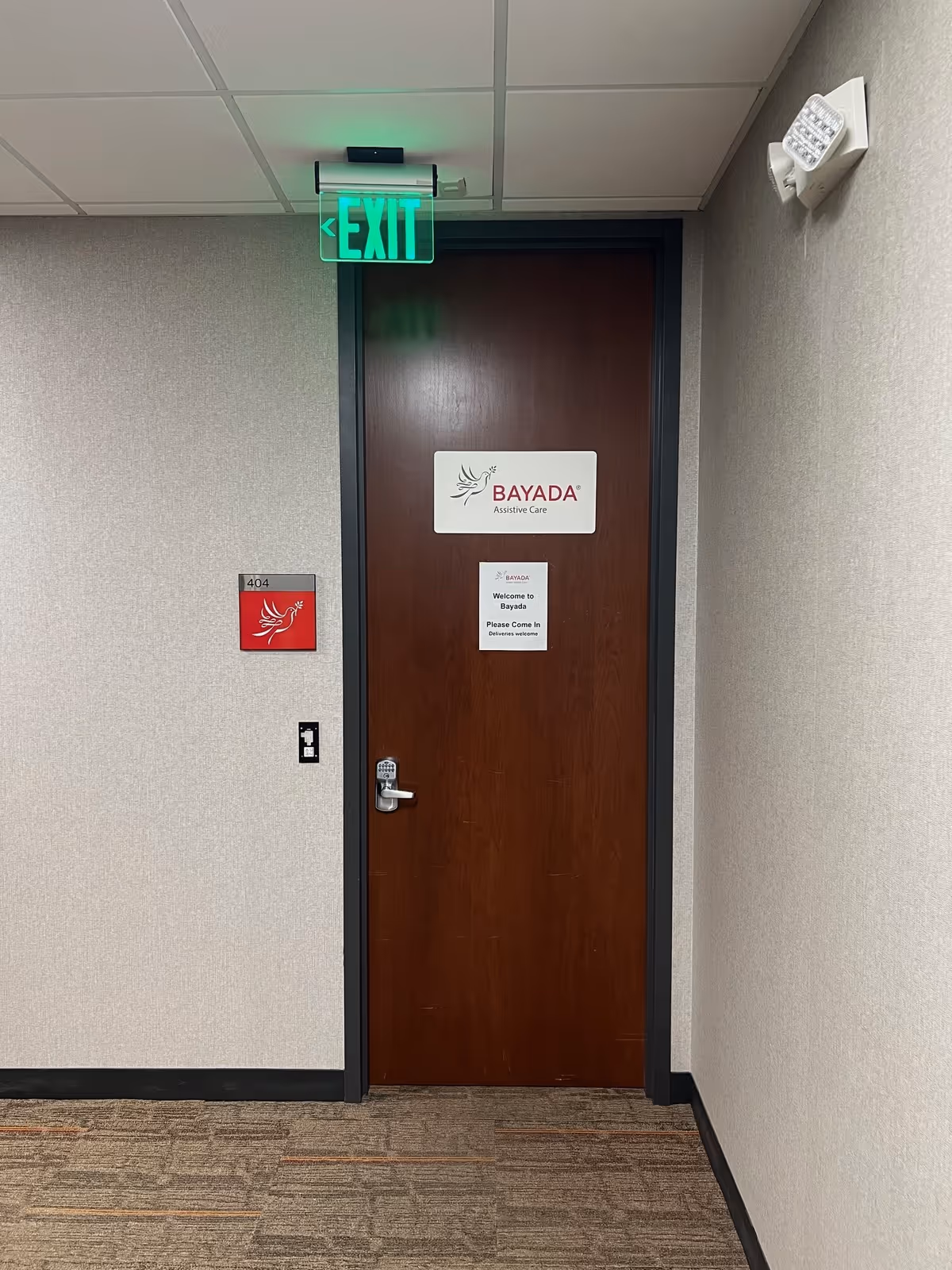 Interior hallway featuring a BAYADA Assistive Care door and illuminated exit sign