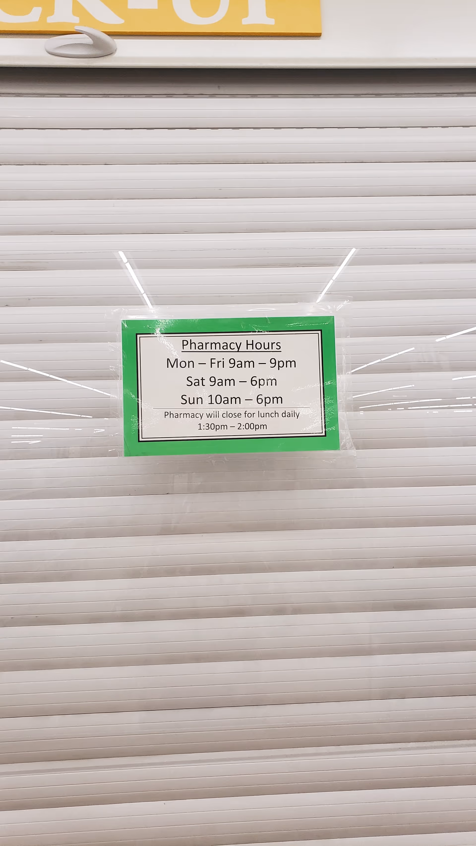 Discount Drug Mart storefront shutter with a green-framed pharmacy hours sign taped on