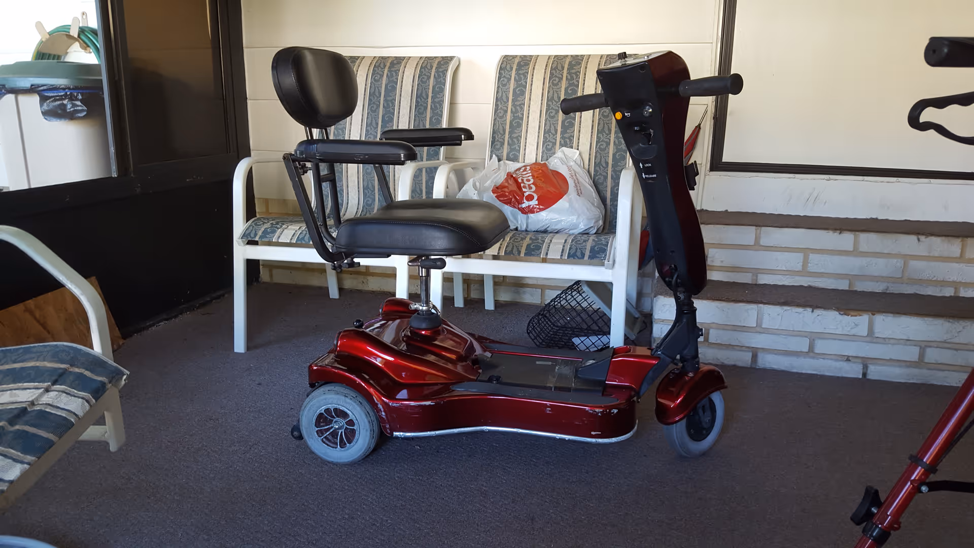 Red mobility scooter on a covered outdoor patio with striped chairs.