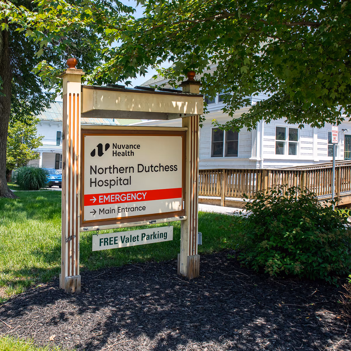 Wood-framed sign for Nuvance Health Northern Dutchess Hospital outside with building facade in background.