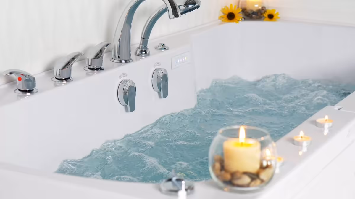 White walk-in tub with chrome fixtures, bubbling water, and candles with sunflowers nearby.