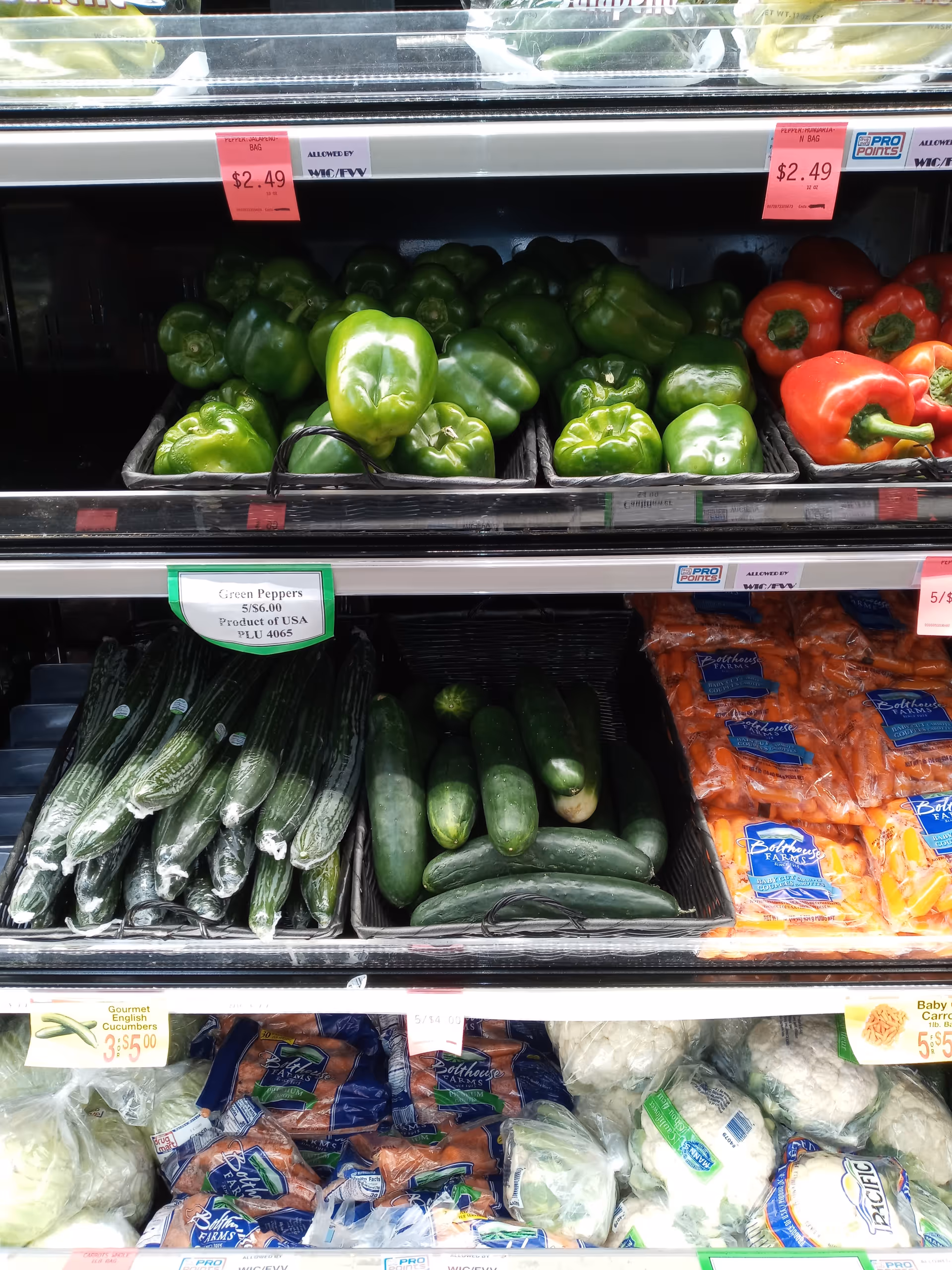 Produce section in a Discount Drug Mart interior with green bell peppers, cucumbers, and carrots.