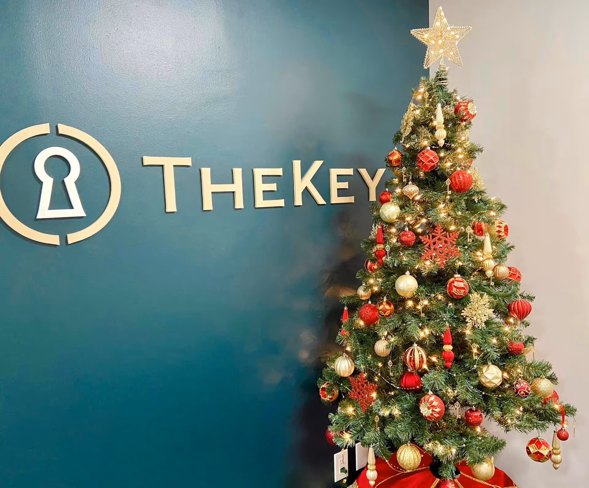 Teal wall with TheKey logo beside a decorated Christmas tree indoors