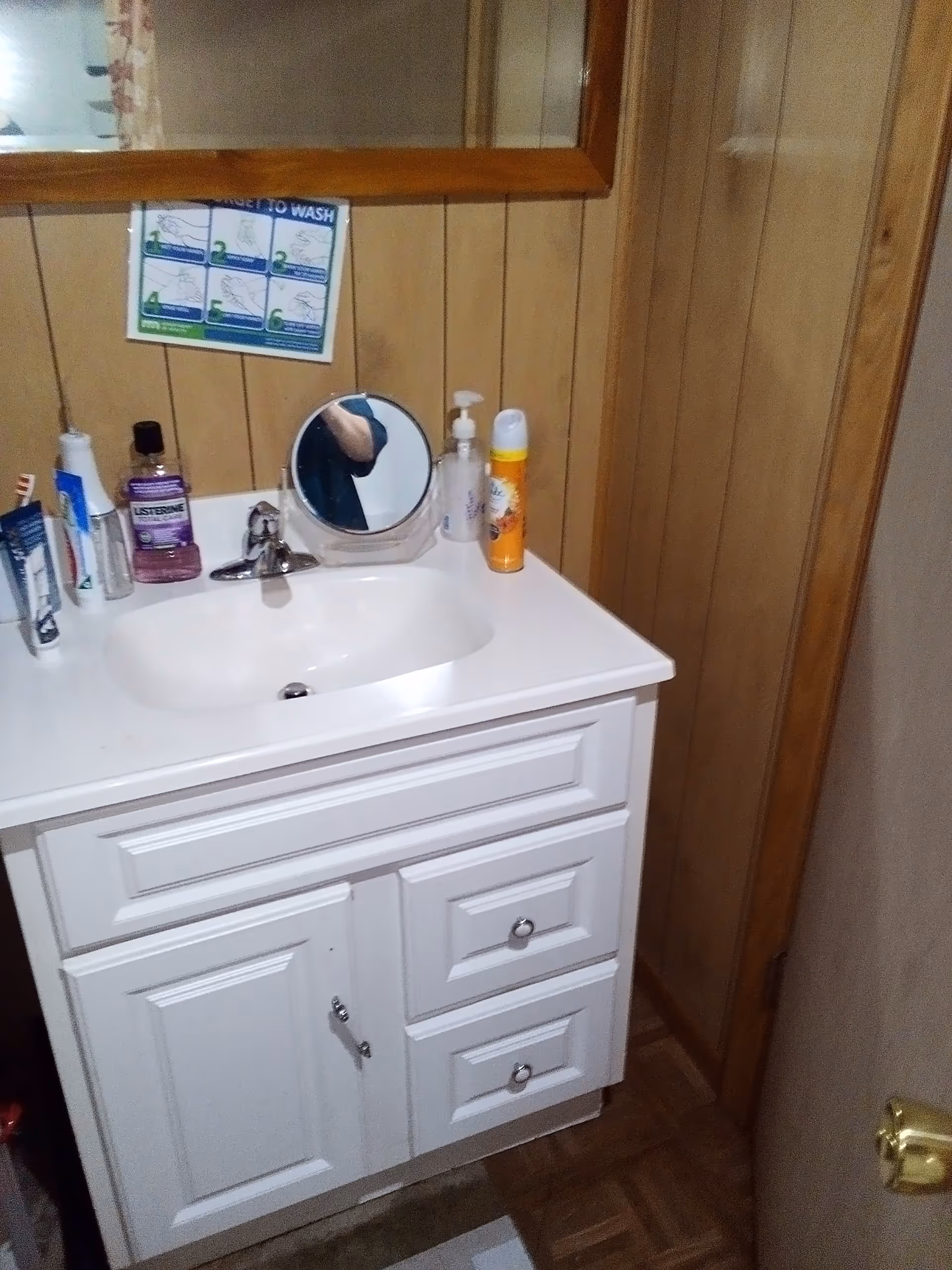 White bathroom vanity with sink and mirror, wooden panel walls, toiletries on the counter.