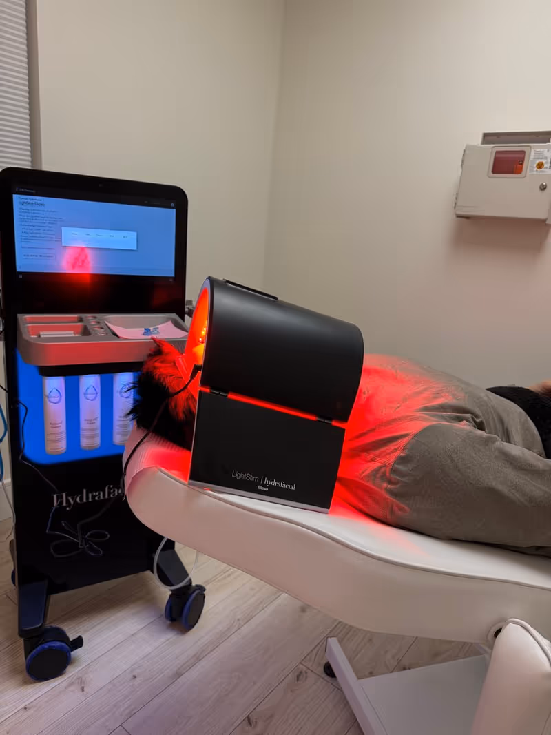 Person lying on treatment table with red light device and monitor nearby.