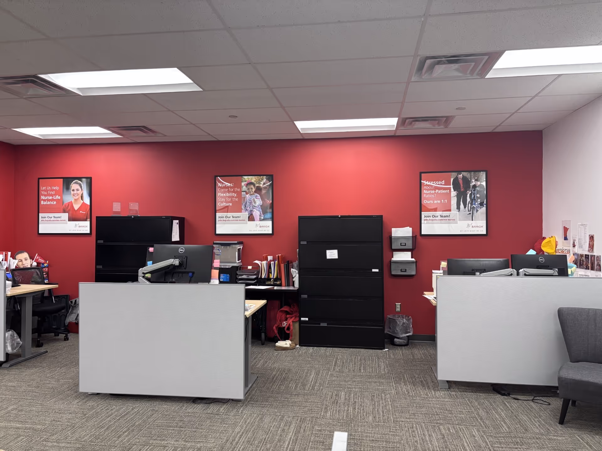 Office reception area with desks, filing cabinets, and posters on a red wall.