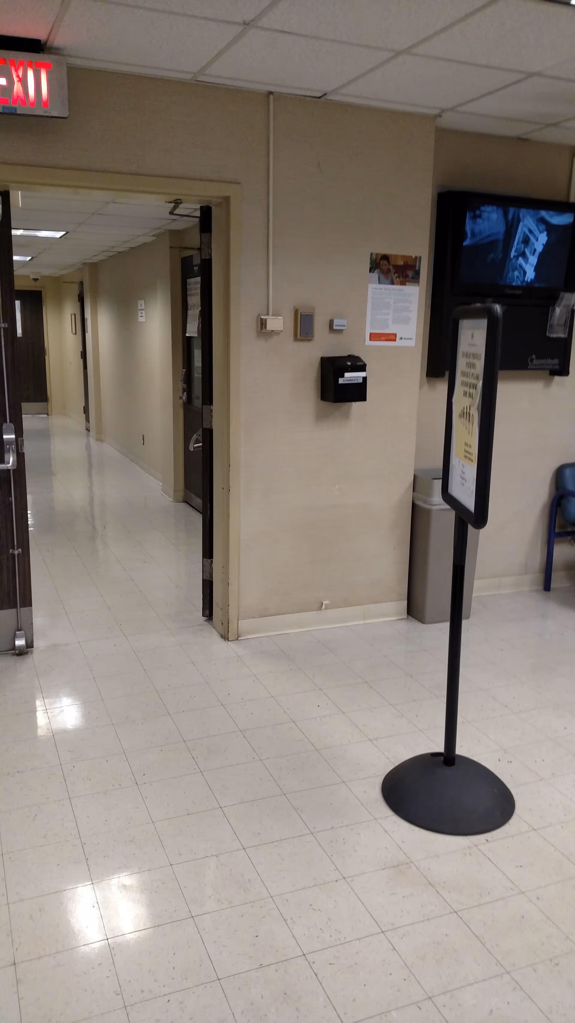 Interior hallway of a senior facility with doors, a TV, and a standing information sign.