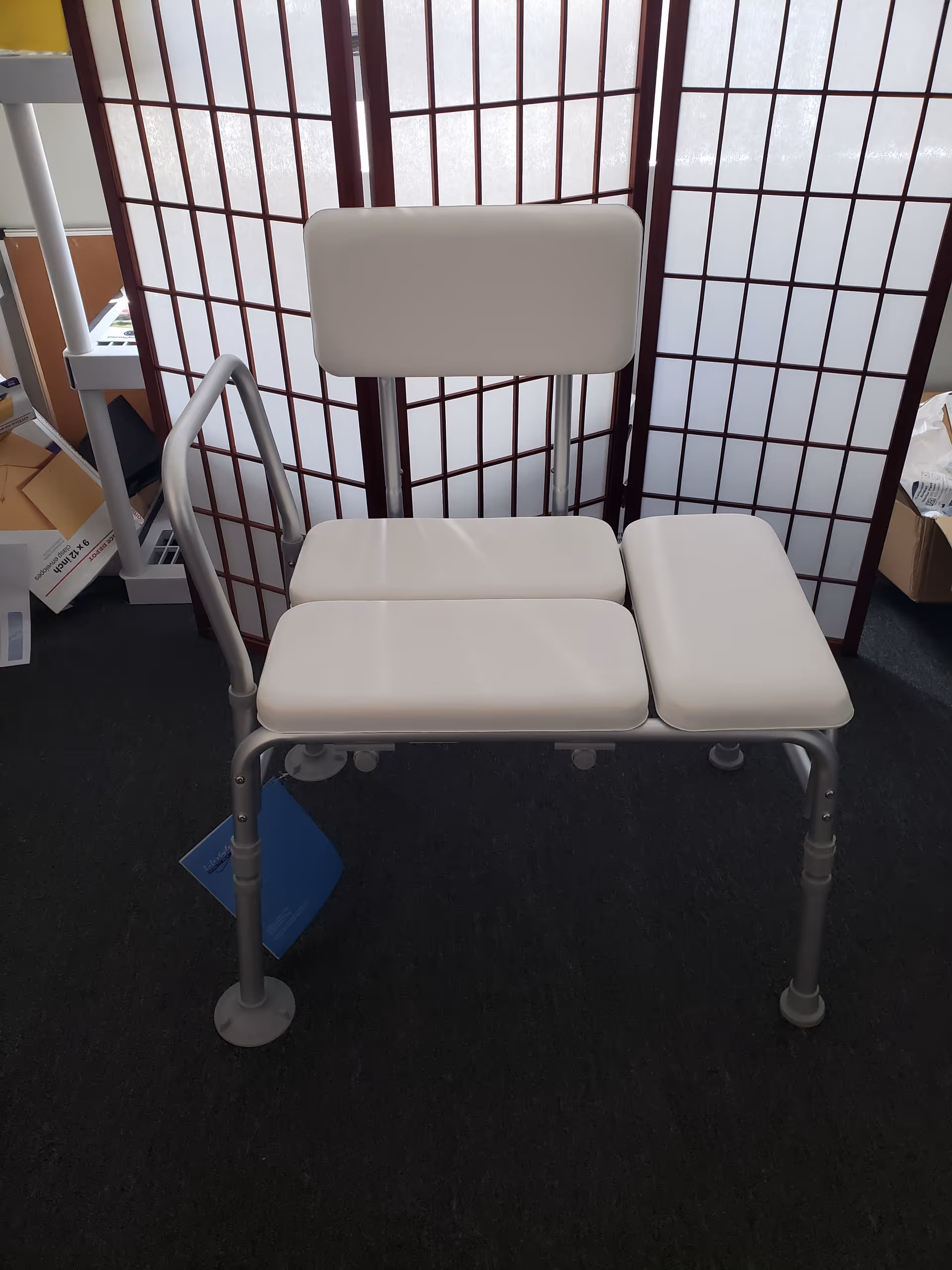 White medical transfer chair with armrest and backrest in front of a folding privacy screen.