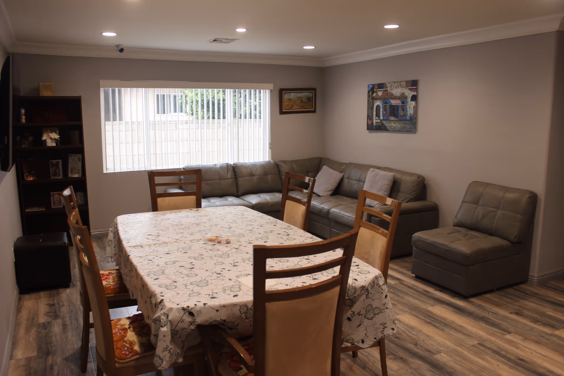 Cozy dining area with a long table, floral tablecloth, and gray sectional sofa along back wall.