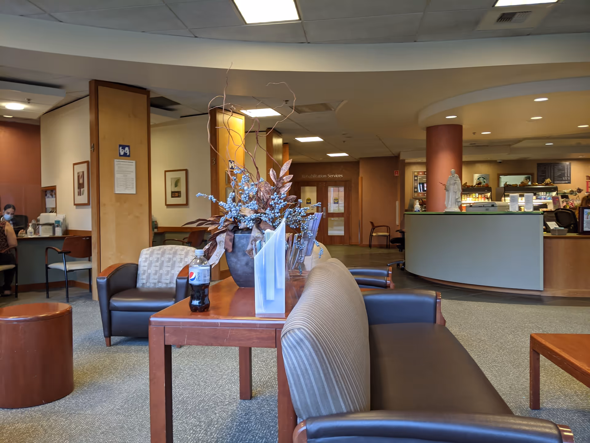 Hospital lobby seating area with couches, tables, plants, and a reception.