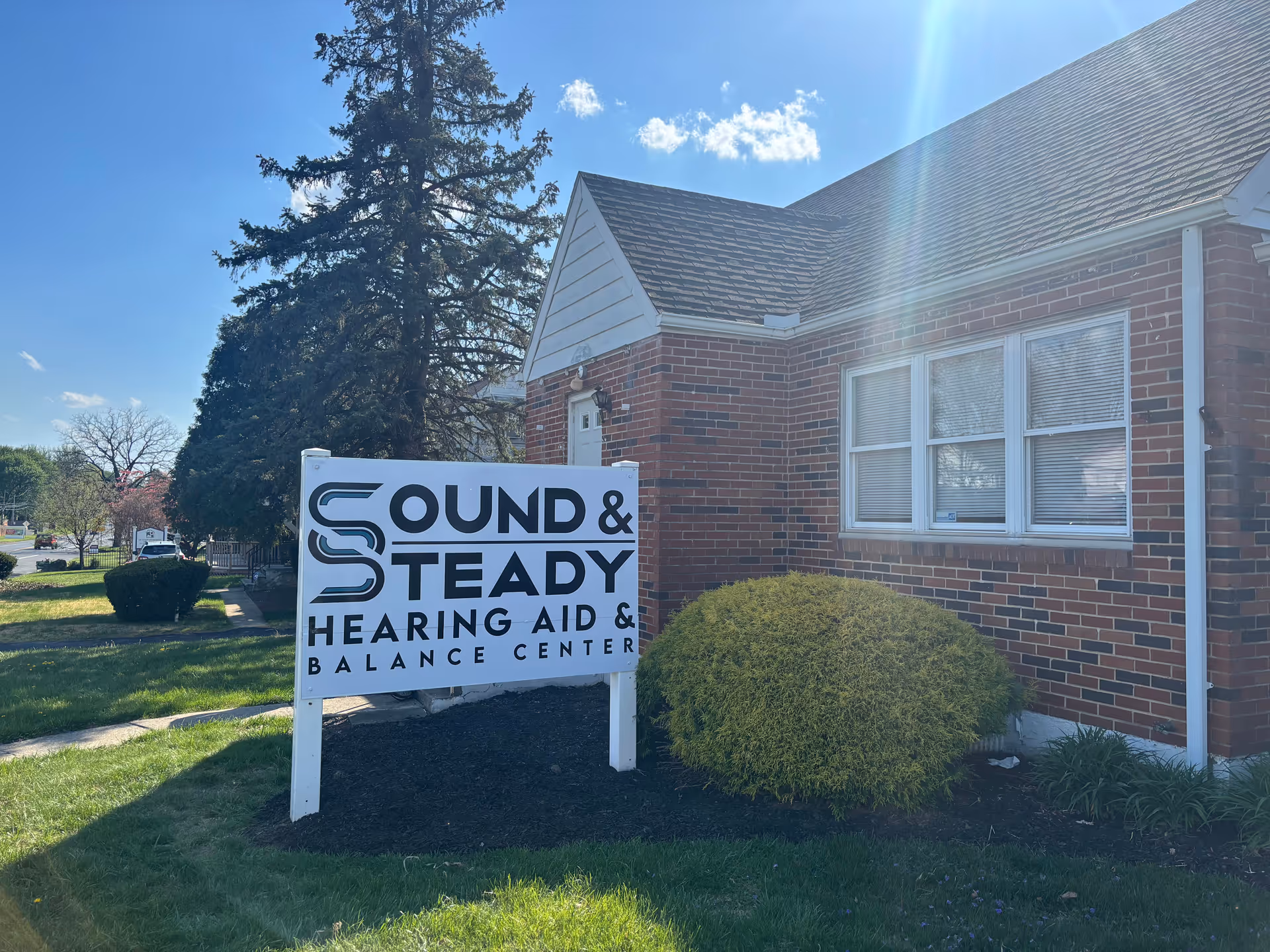 Exterior brick building with a large white sign for Sound & Steady Hearing Aid.