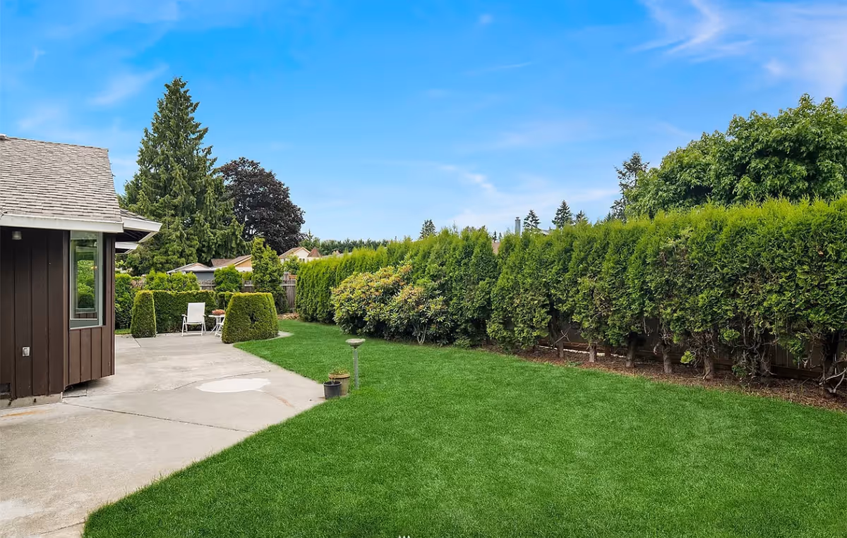 Green lawn, hedges, and a small patio area beside a brown building.