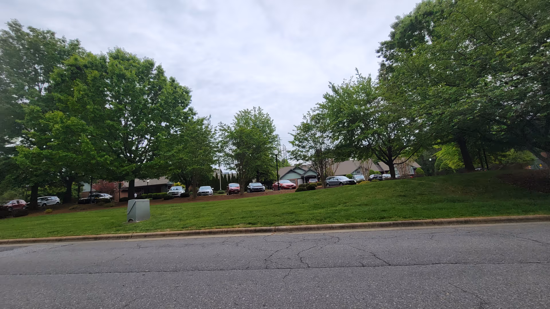 Exterior view of Trellis Supportive Care showing a grassy slope, trees, and parked cars along street.