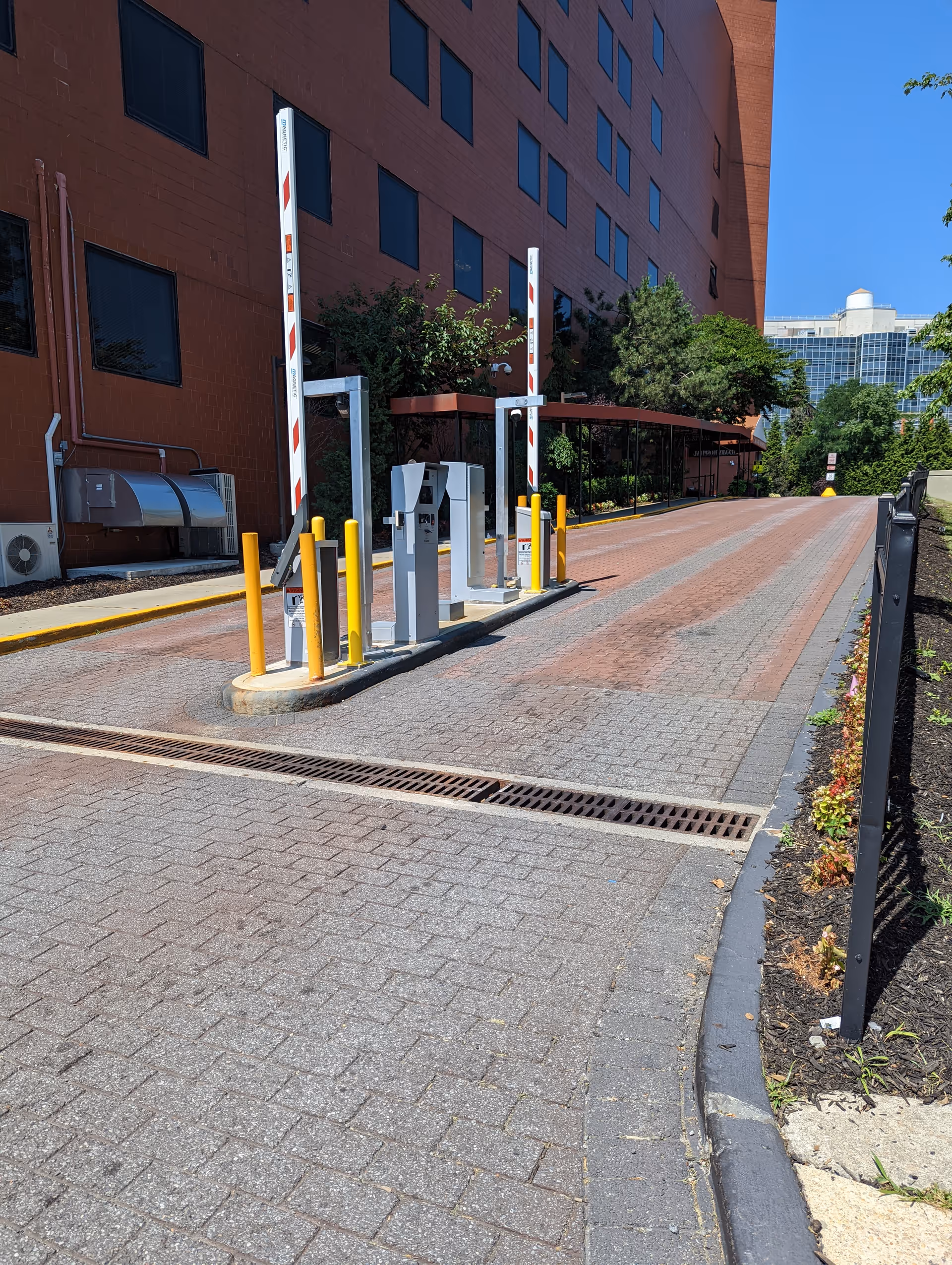 Outdoor hospital entrance with barrier gates, striped posts, and a brick building.