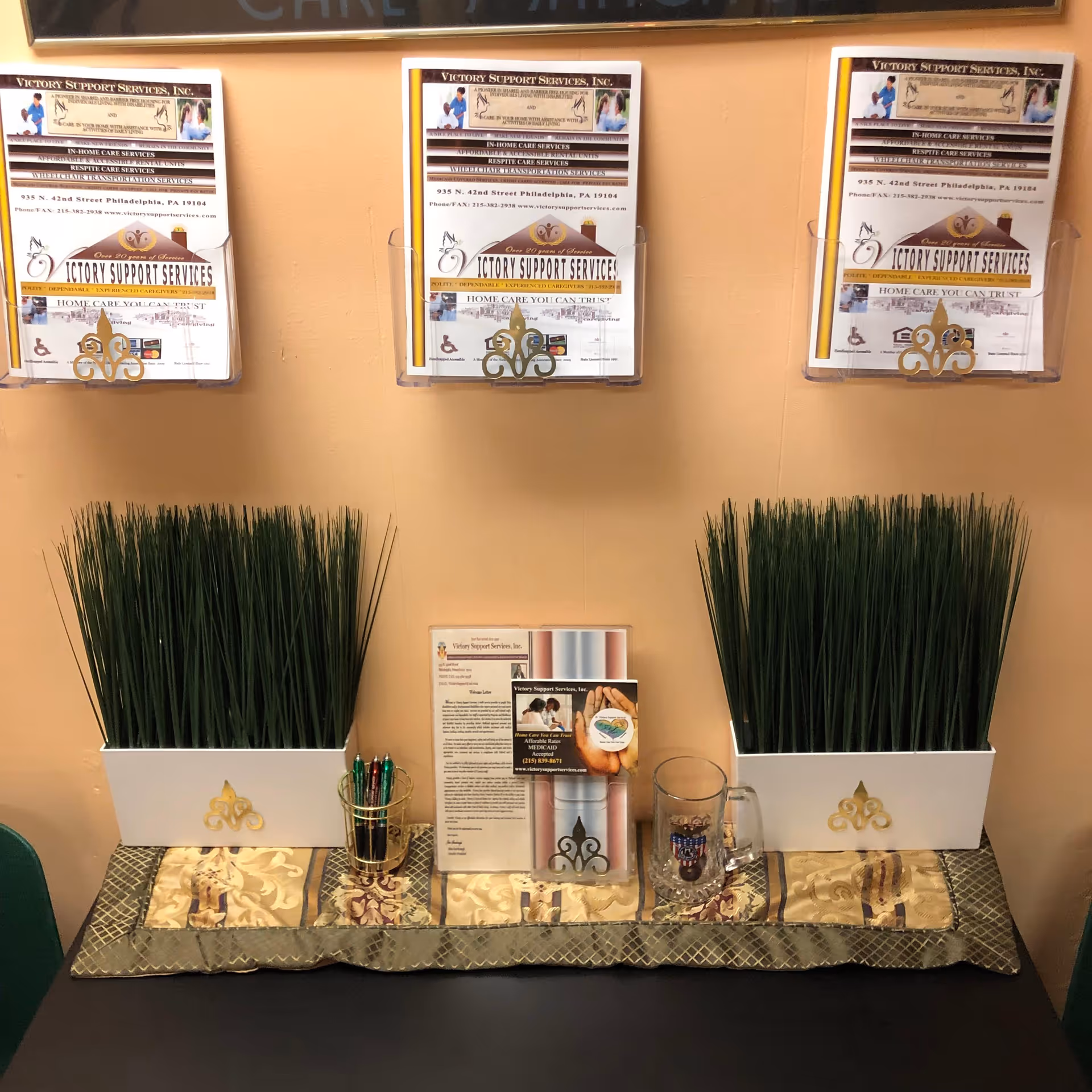 Lobby front desk area with brochures, two white planters, pens, mug, and decorative runner.