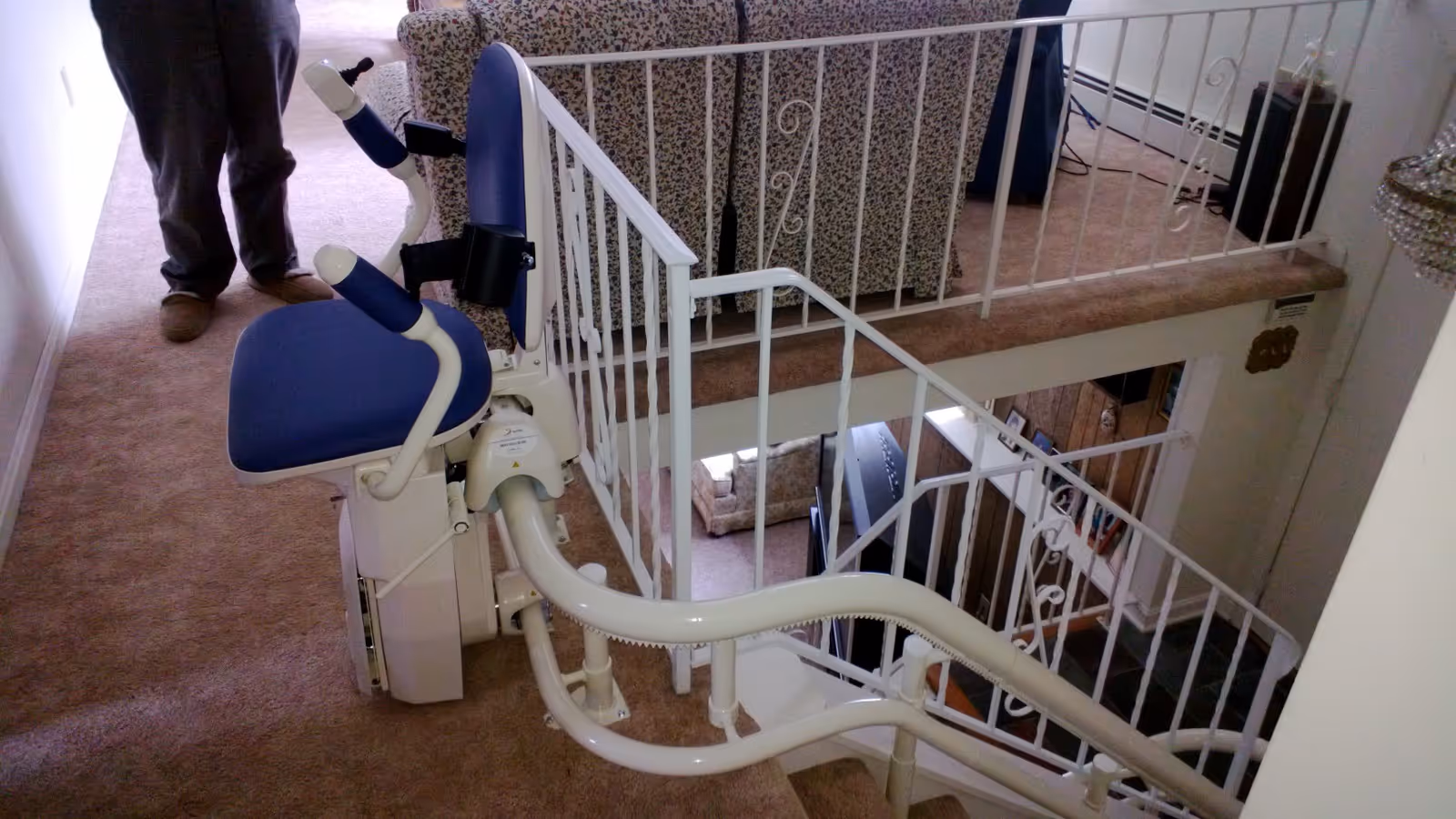 Indoor stair lift installed along a carpeted staircase with white railings and furniture nearby.