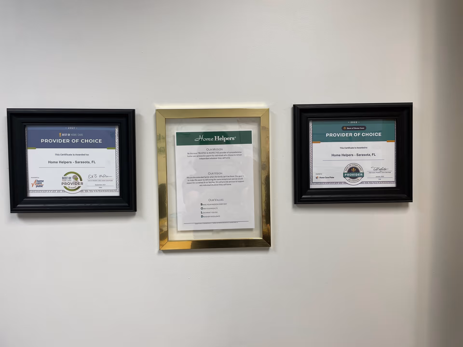 Three framed awards hung on a white wall in a facility hallway.