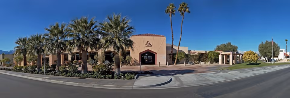 Beige single-story building with a welcoming entrance, palm trees, and a curved road in front