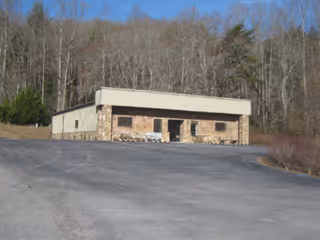 Front view of a stone-clad, single-story building with a spacious parking lot.