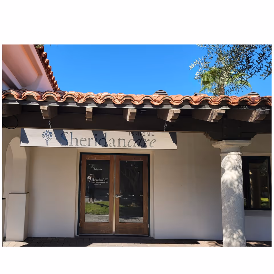 Front view of SheridanCare entrance with clay tile roof and wooden doors under blue sky.