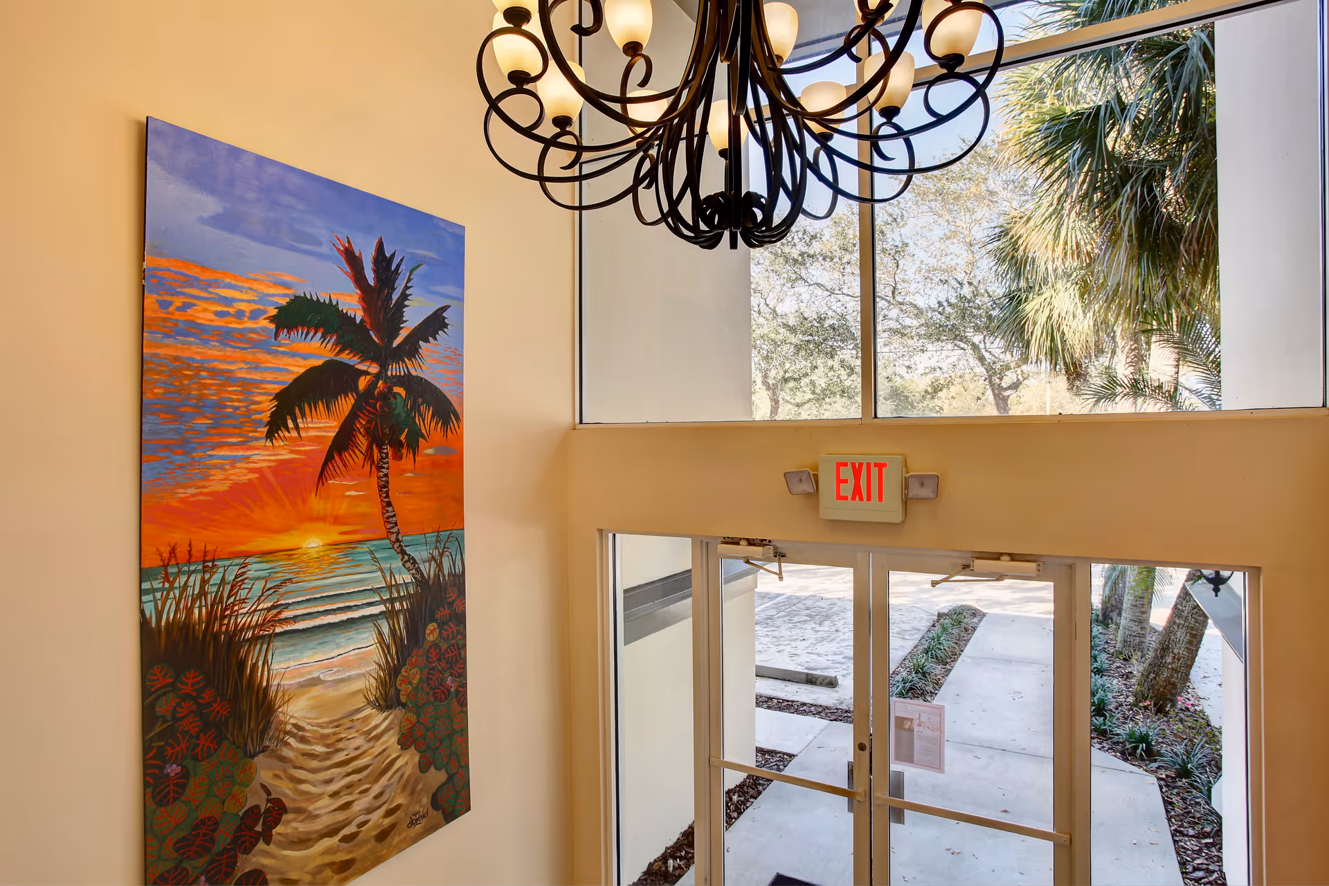Interior lobby with exit doors, chandelier, vibrant painting, and outside view.