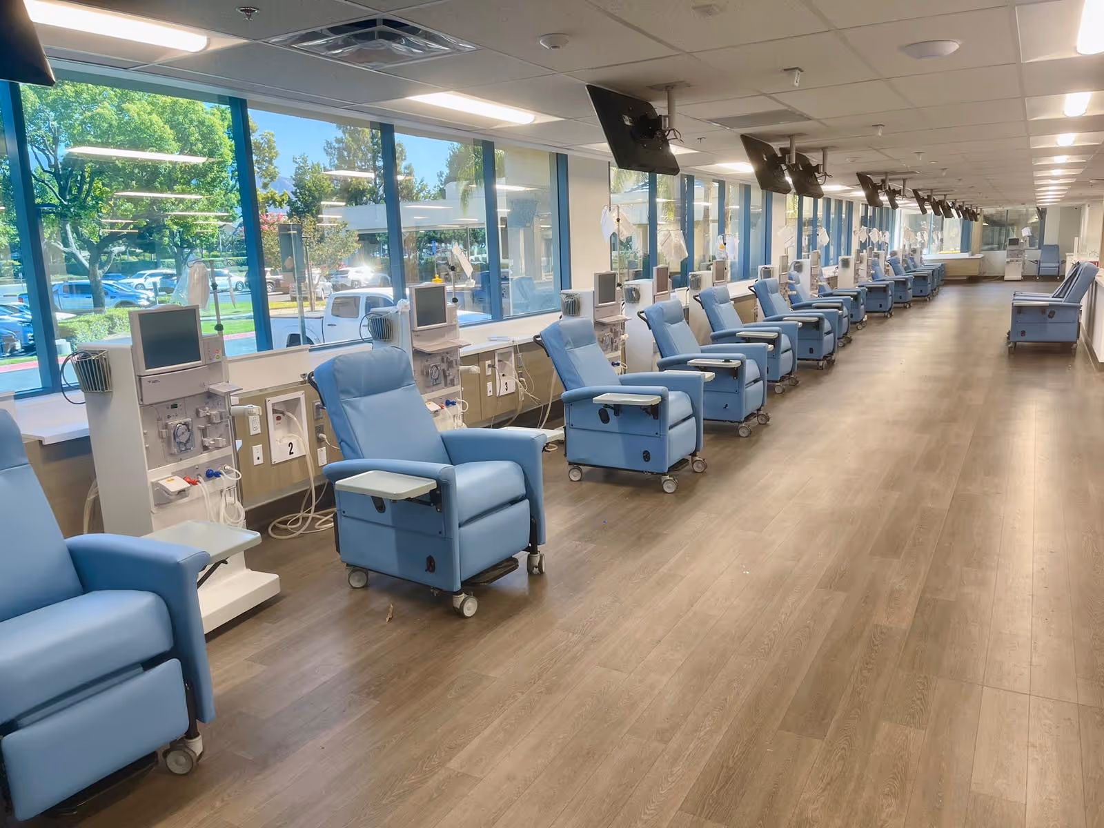 Long dialysis treatment room with blue chairs and medical machines along windows