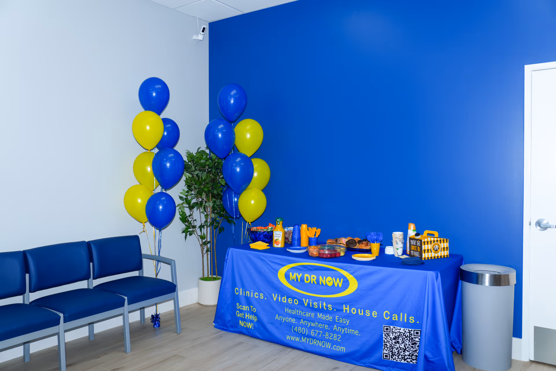 Interior with a blue accent wall, MY DR NOW refreshments table, balloons, and seating.