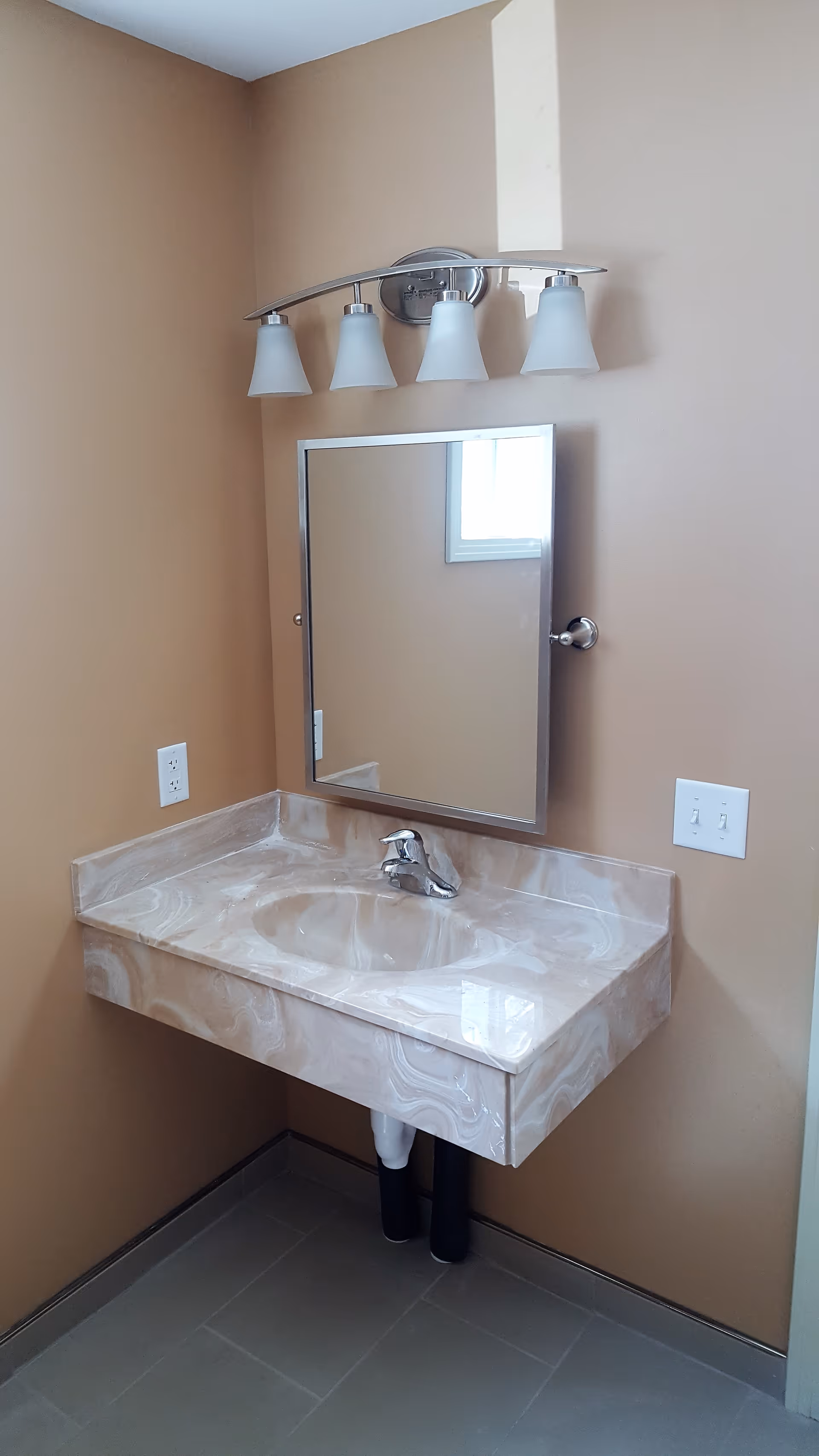 Beige bathroom with marble sink, wall-mounted mirror, and a four-light vanity fixture.