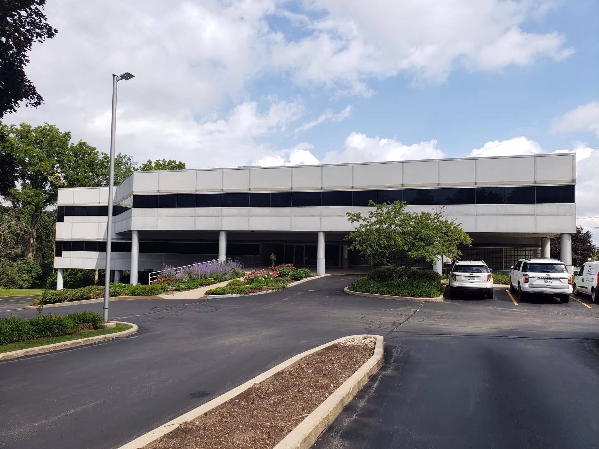 Front view of a modern, two-story hospice facility with parking and landscaped entrance.