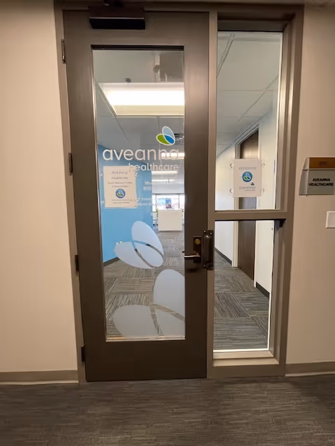Glass entry door opens to Aveanna Healthcare interior with blue logo walls.