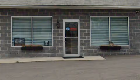 Front exterior of a brick building with two windows and a central door.