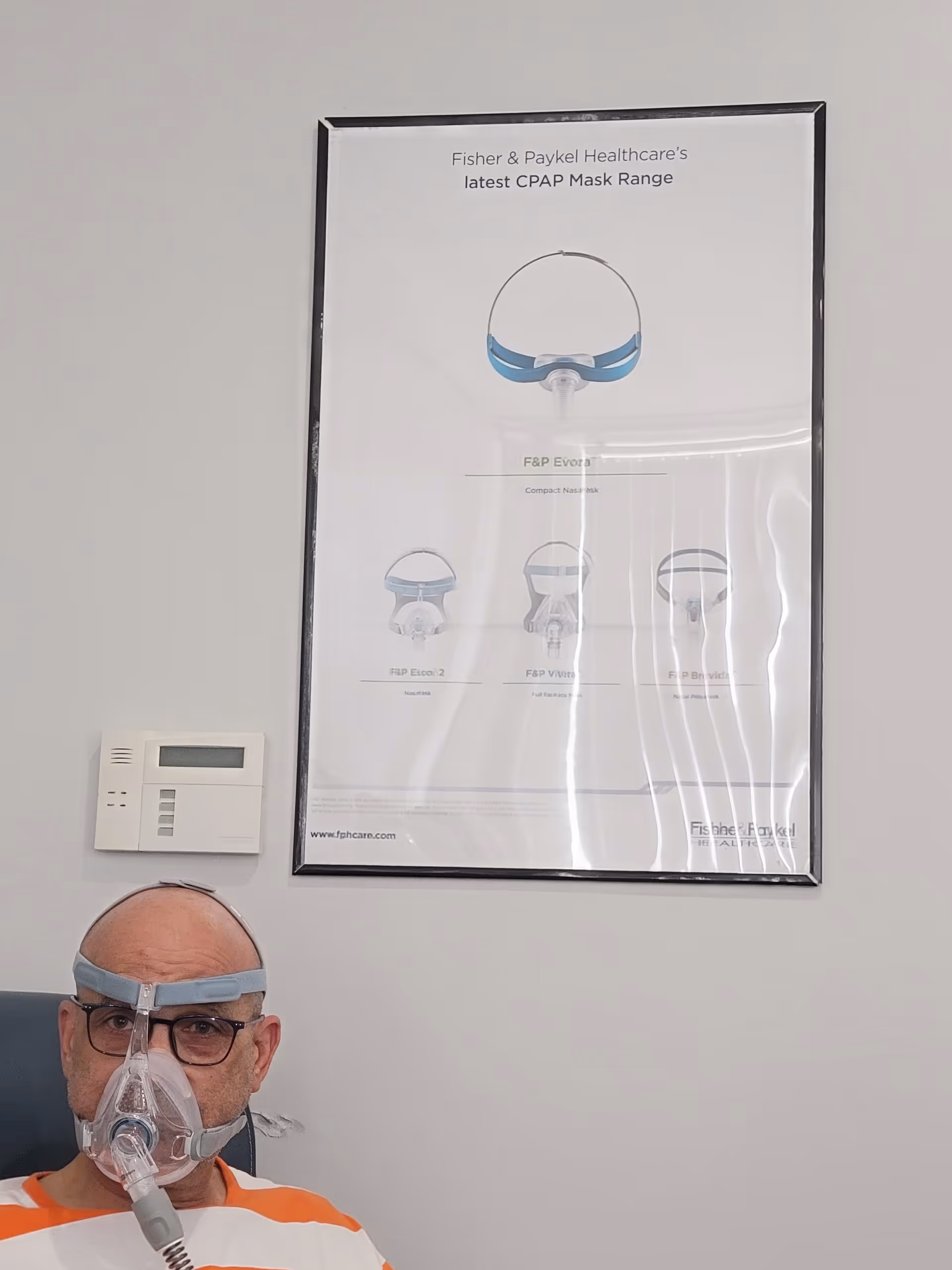Resident wearing a CPAP mask seated in a LINCARE interior beside a medical poster.
