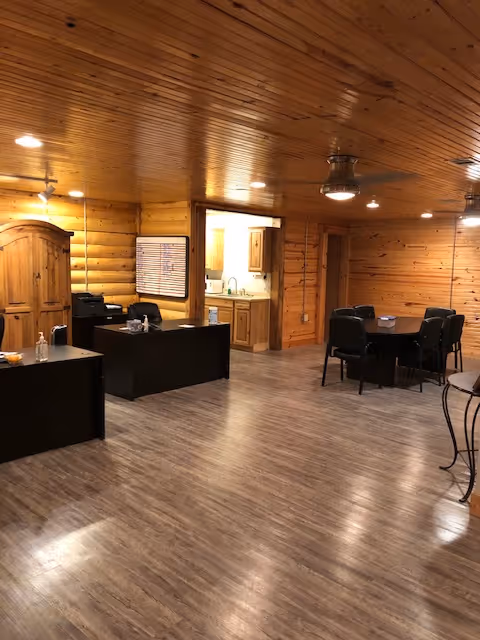 Interior of a rustic wood-paneled senior living common area with dining tables and a kitchenette.
