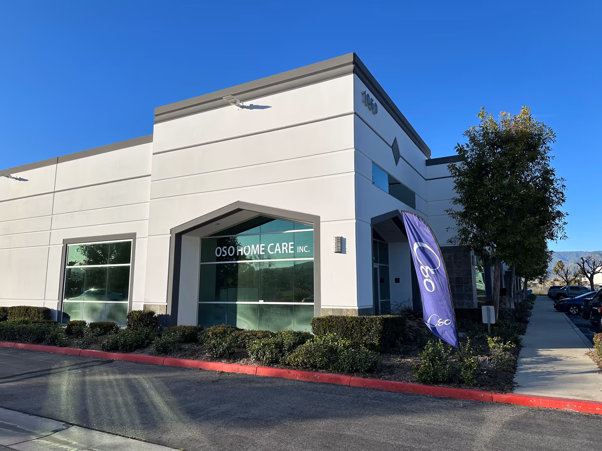 Exterior view of OSO Home Care building with sign, plants, and purple flag