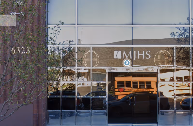 Glass entrance of building with reflections of cars and a school bus, ivy on the left.