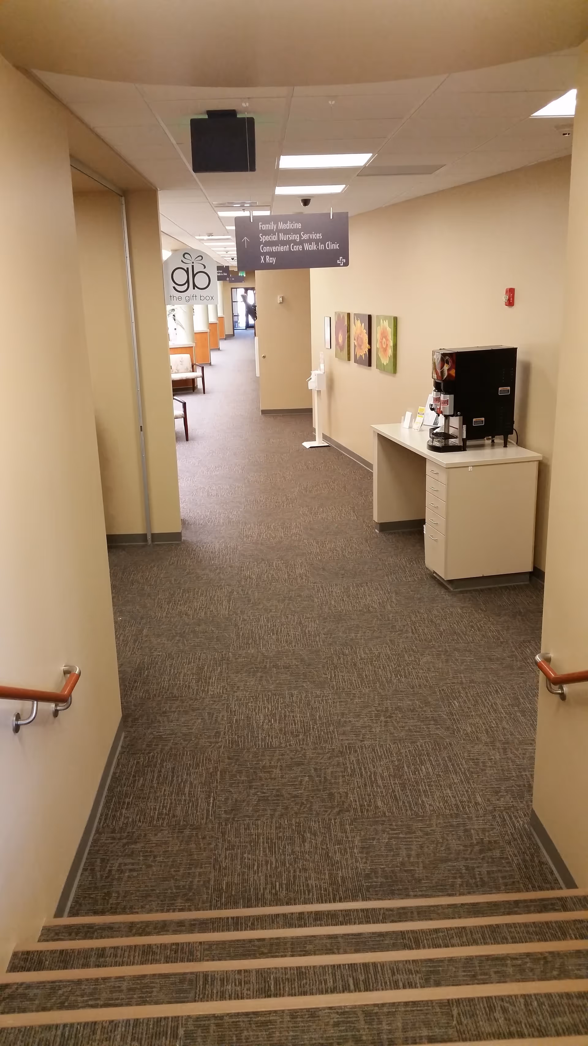 Long beige hallway in a senior living facility with a coffee station and stairs.