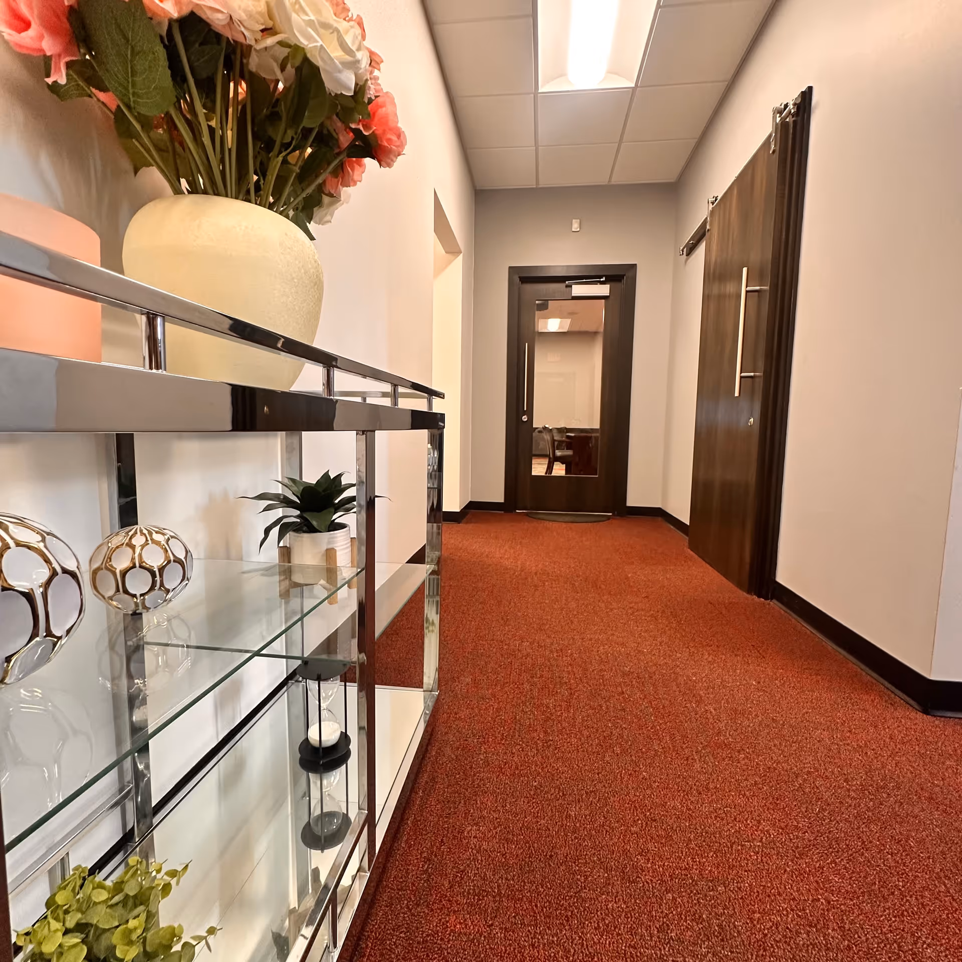 Hallway inside a senior living facility with red carpet, glass shelves, and closed doors.