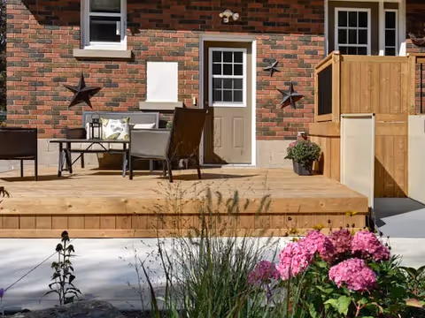 Wooden outdoor deck with seating area and flowers against a brick building