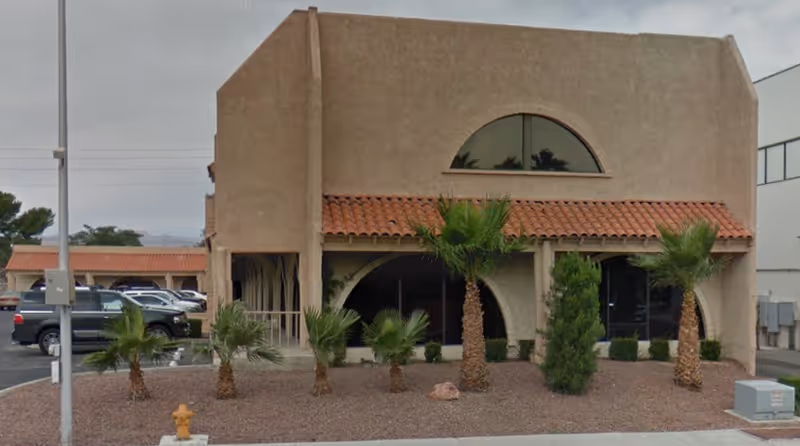 Front view of a stucco building with palm trees and arched entrance.